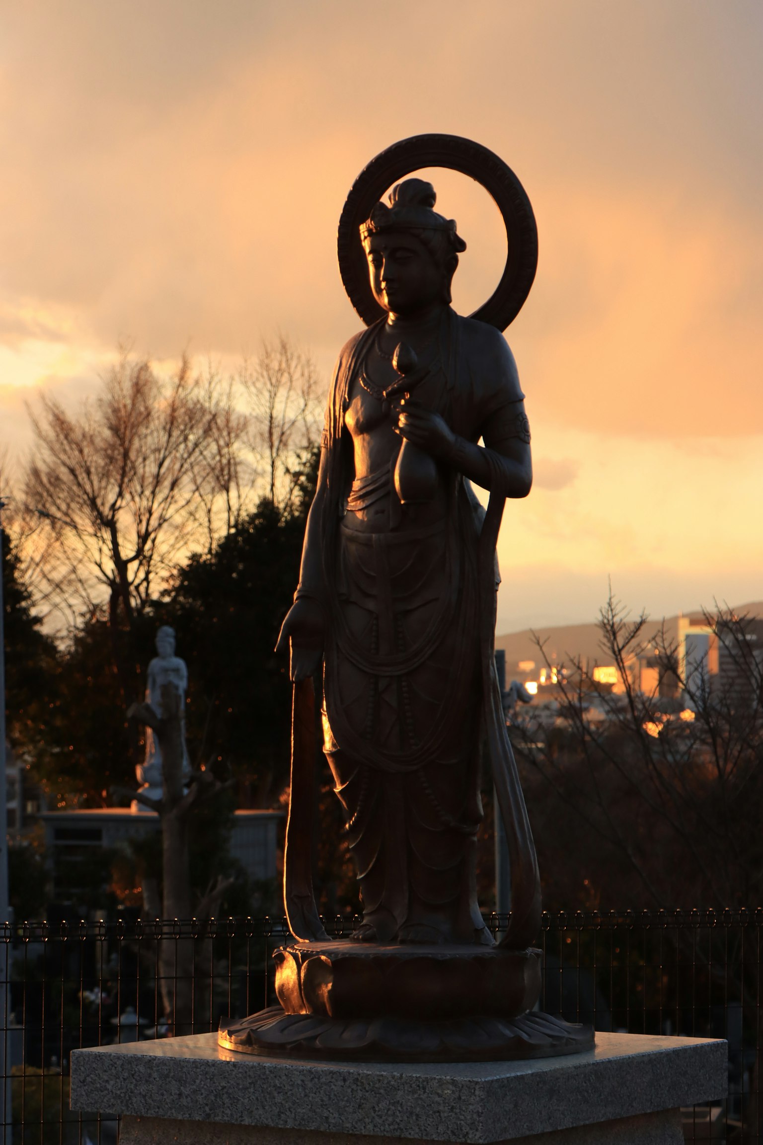 Una statua di una figura con un bastone si erge contro uno sfondo di tramonto