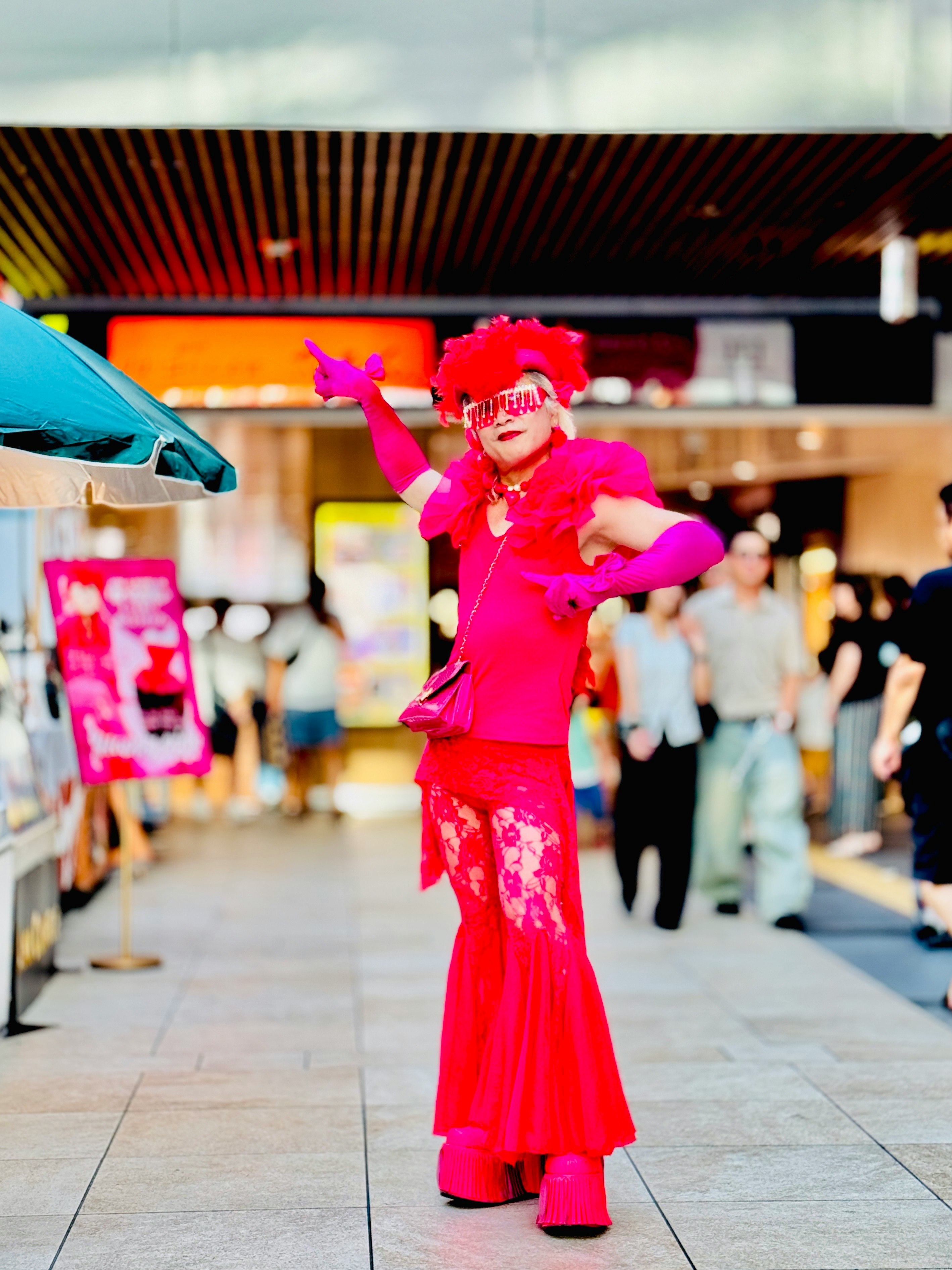 鮮やかなピンクの衣装で踊る人物が商店街の通路にいる