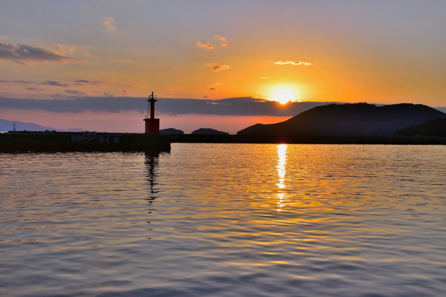 Hermoso atardecer reflejándose en el mar con un faro rojo al fondo