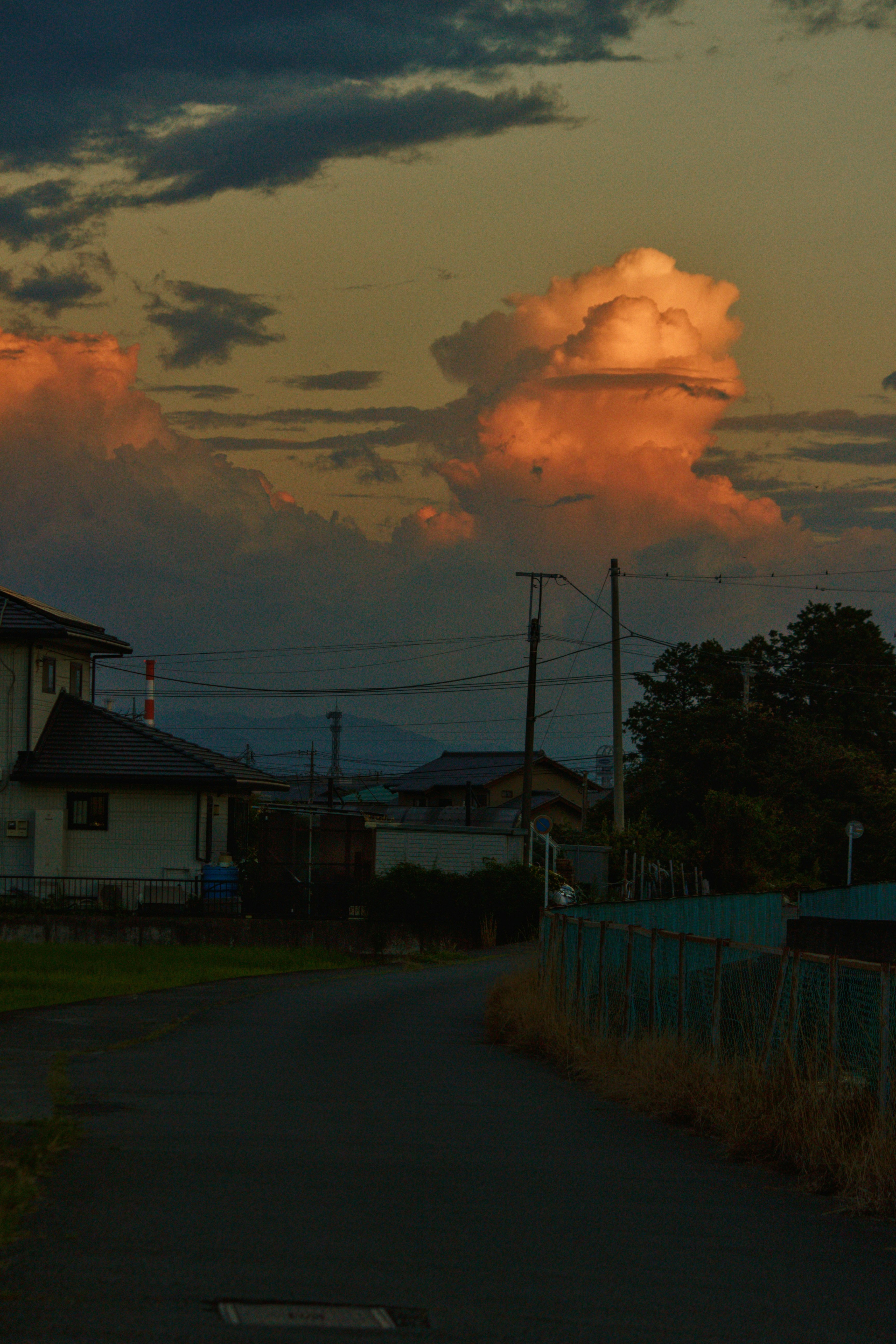 夕方の雲と工場の煙突が見える郊外の道沿いの風景