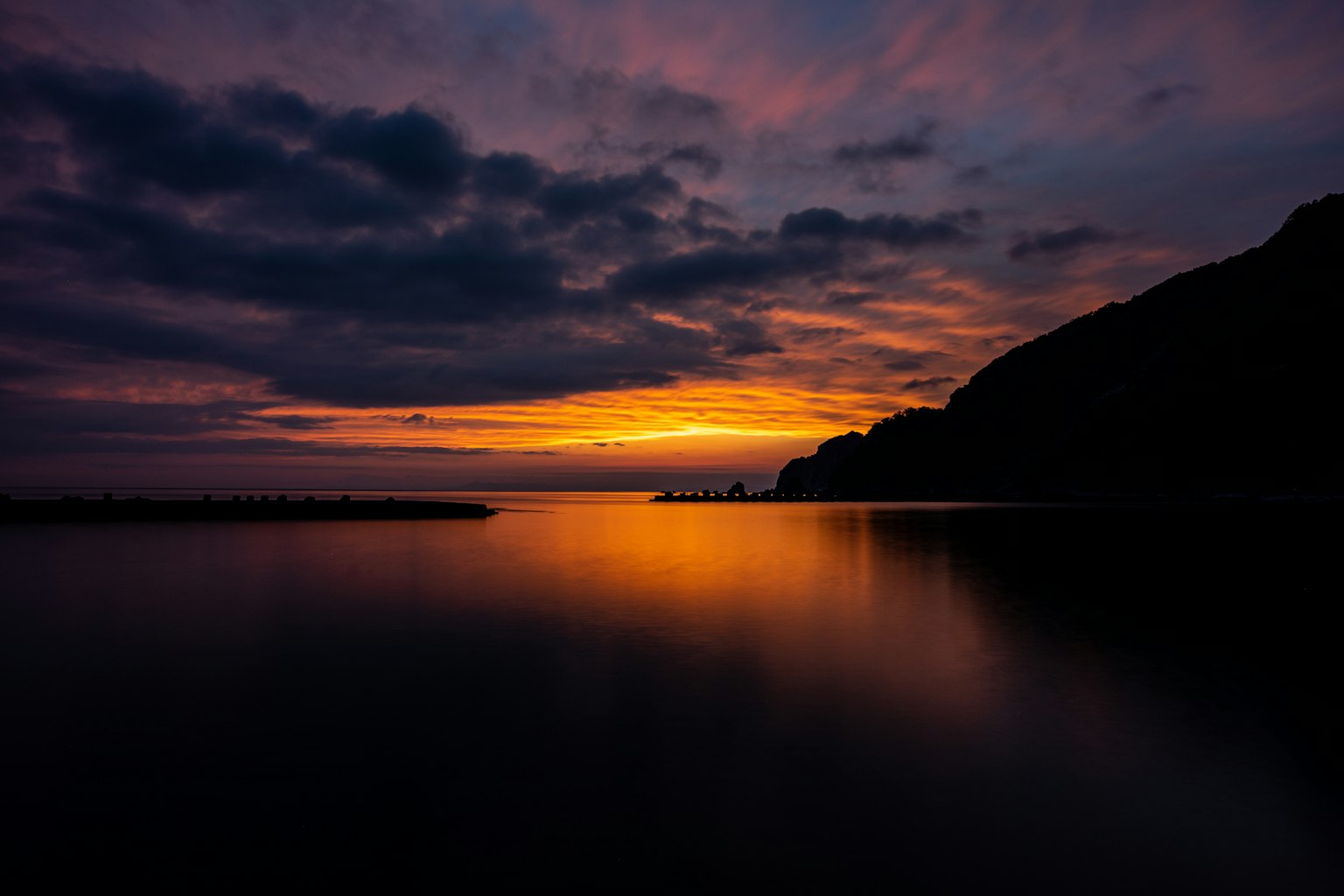 美しい夕焼けが海に映る静かな風景 山と雲がシルエットとして浮かび上がる