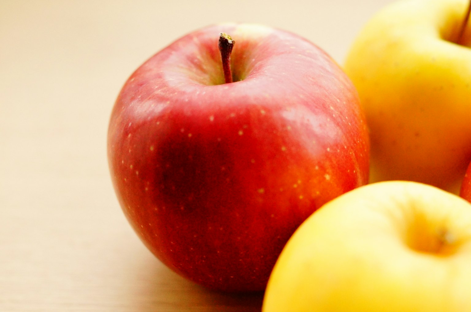 Une pomme rouge vibrante à côté de pommes jaunes sur un fond clair
