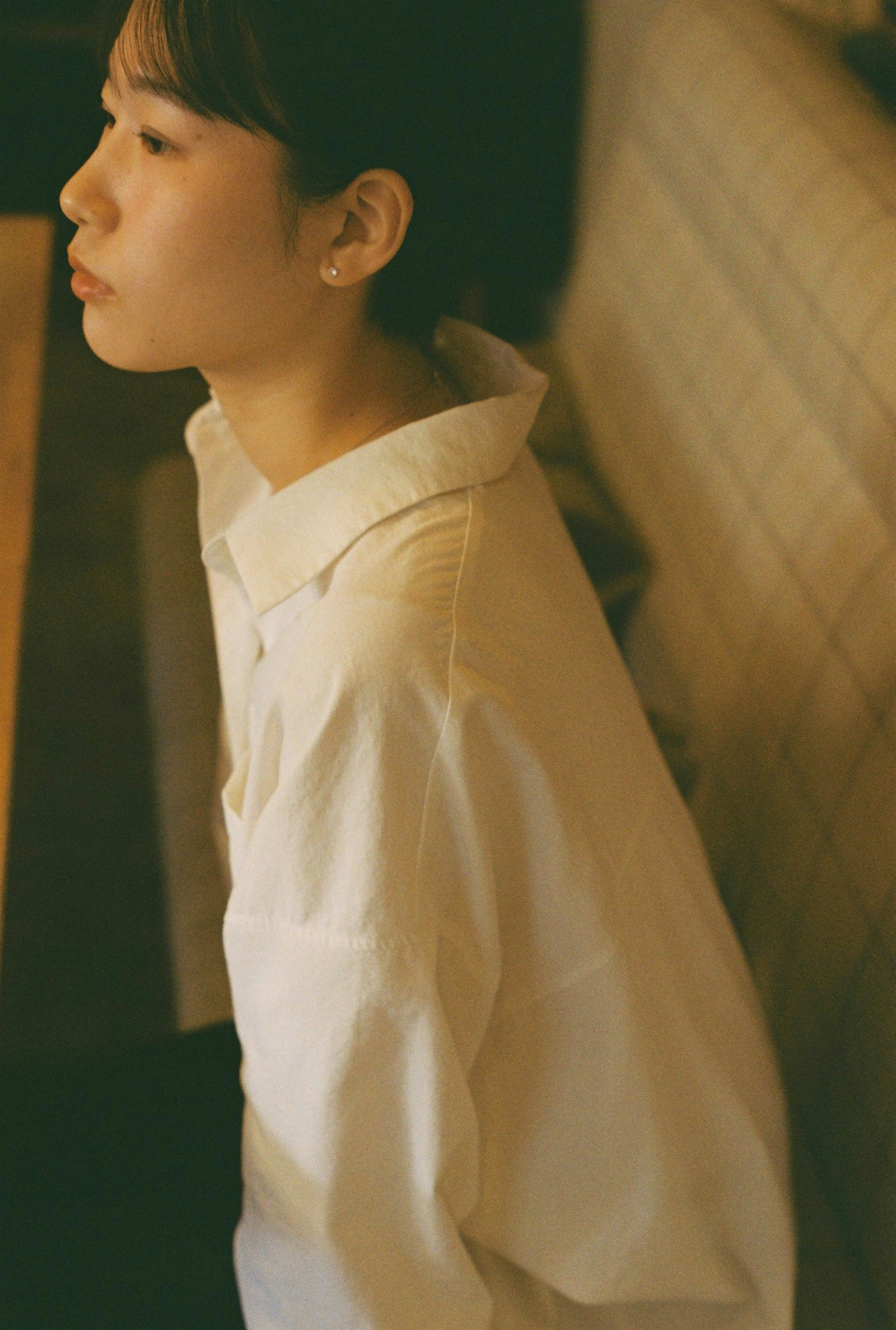 横向きに座っている女性のポートレート 白いシャツを着ている 柔らかい照明の中での静かな瞬間