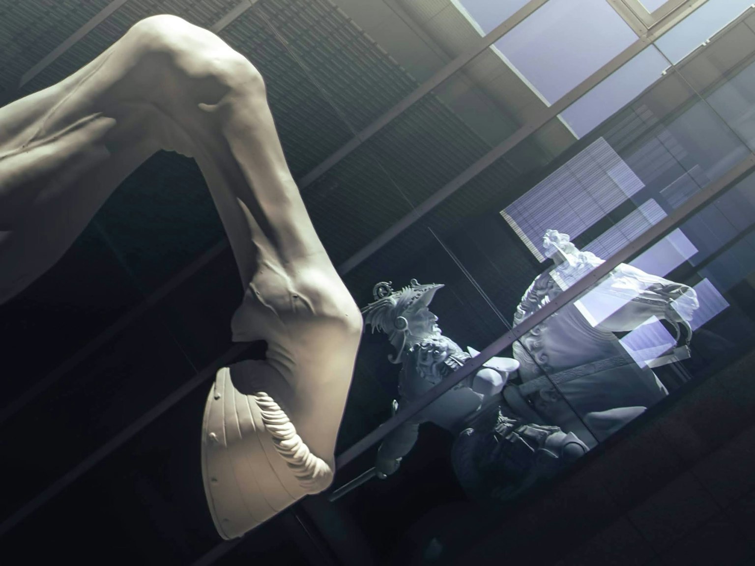 A smooth white arm from a sculpture emerges against a dark background with light streaming through a window