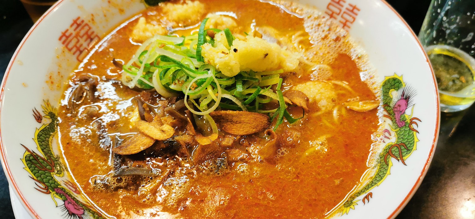 Ciotola di ramen con brodo rossastro guarnita con cipolle verdi e vongole