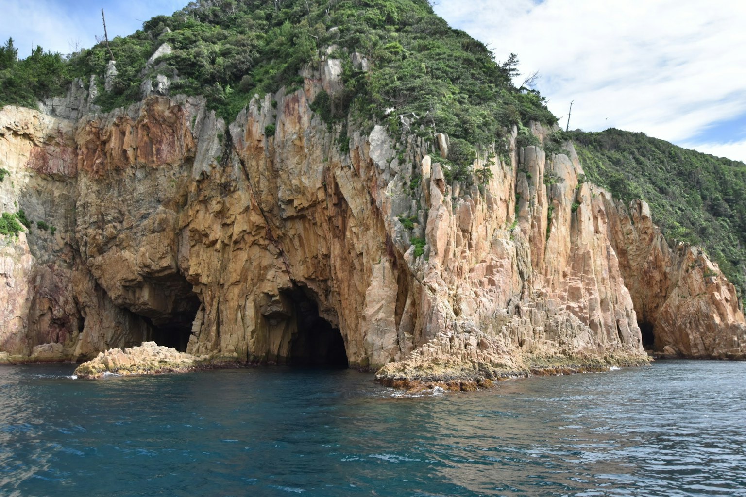 Hang đá bao quanh bởi nước xanh và cây cối xanh tươi