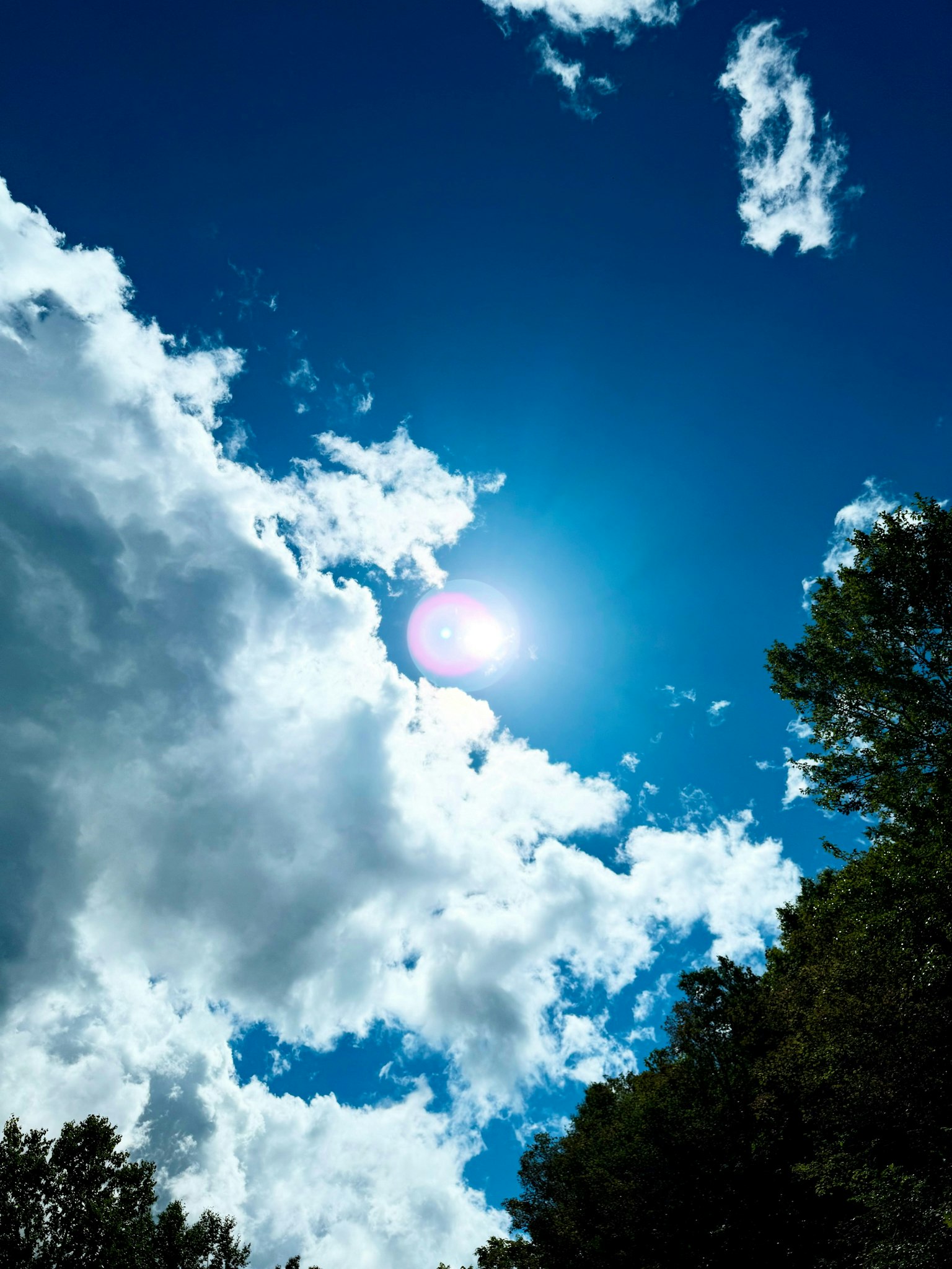 Matahari cerah bersinar melalui awan putih di langit biru