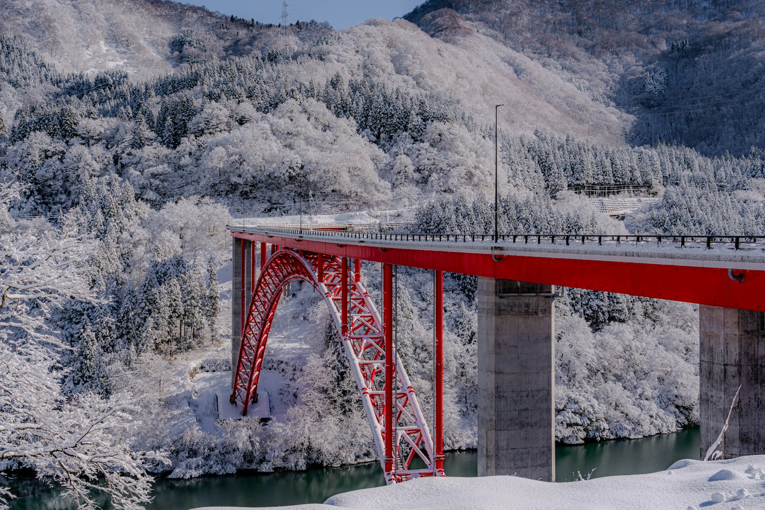 Vista panoramica di un ponte rosso su un fiume circondato da montagne innevate