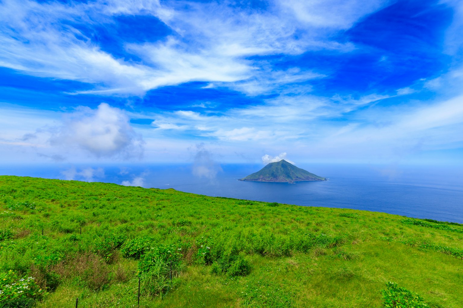 Vibrant green landscape with a volcanic island in the ocean under a blue sky