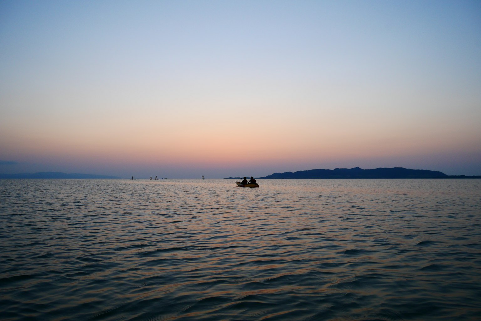 A small boat floating on calm water under a pastel sky