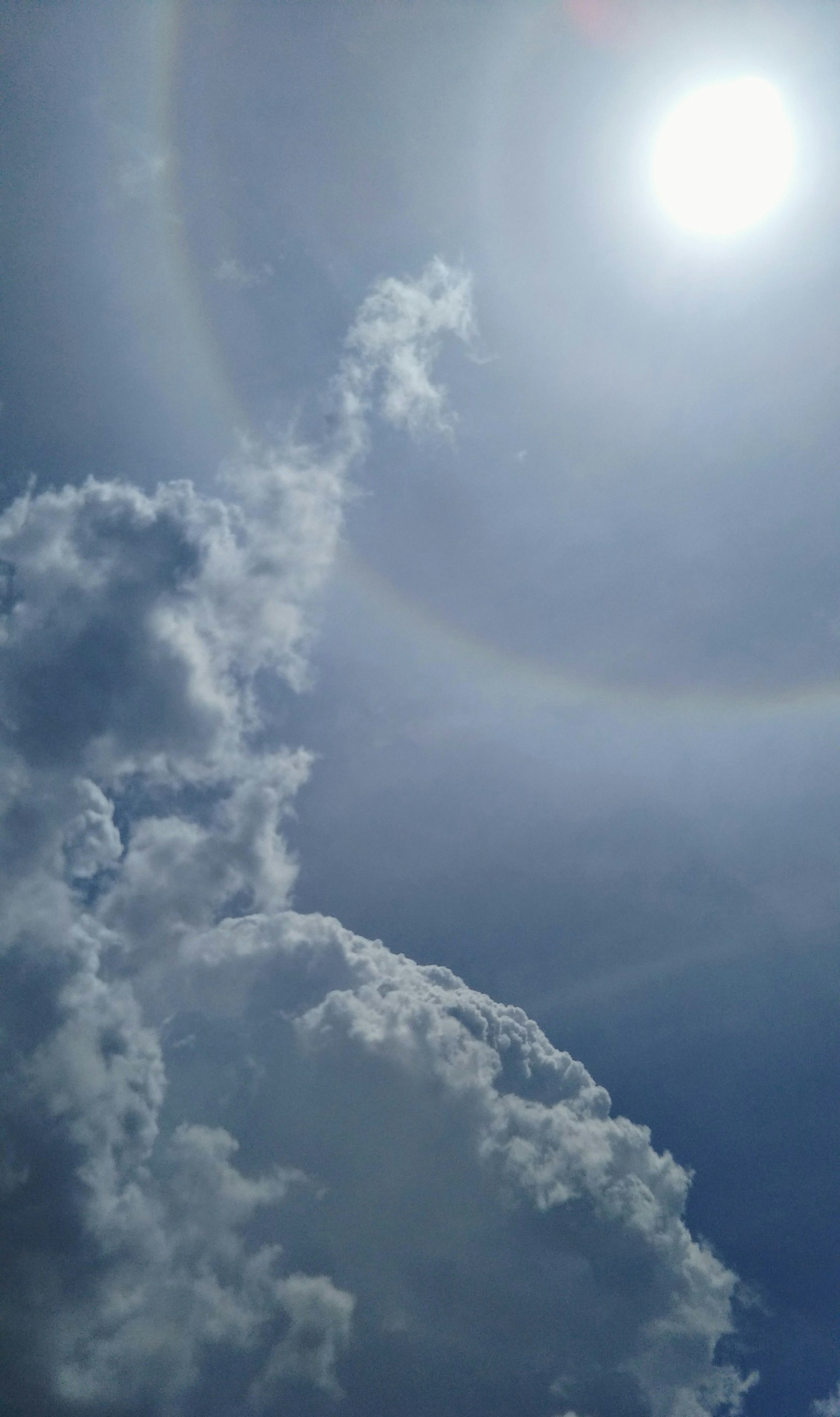 Weiße Wolken in einem blauen Himmel mit einem Halo um die Sonne