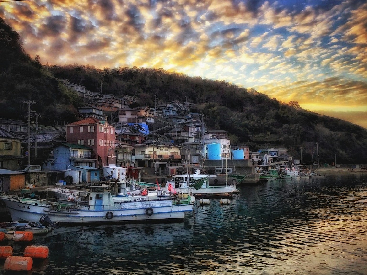 Barche da pesca colorate allineate lungo la costa con un tramonto e colline sullo sfondo