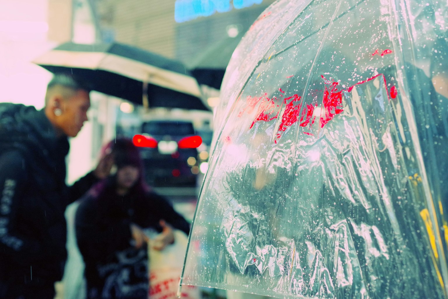 Close-up of a transparent umbrella with people holding umbrellas in the rain