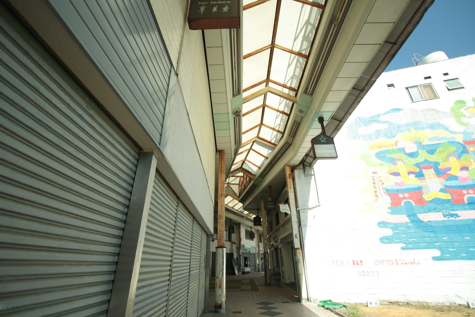 Une rue dans une arcade commerçante avec des vitrines fermées et une fresque colorée sur le mur
