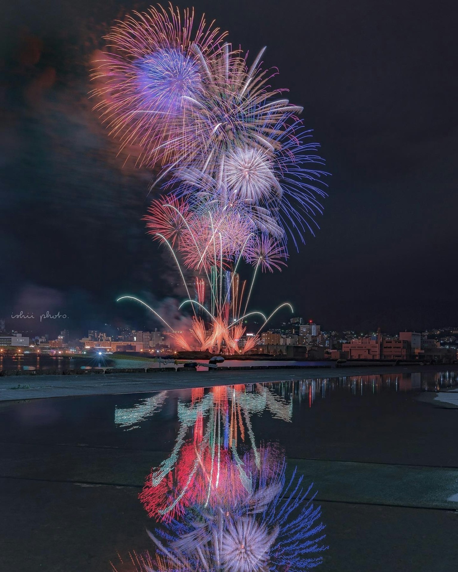 Fuochi d'artificio colorati che esplodono nel cielo notturno riflessi sulla superficie dell'acqua