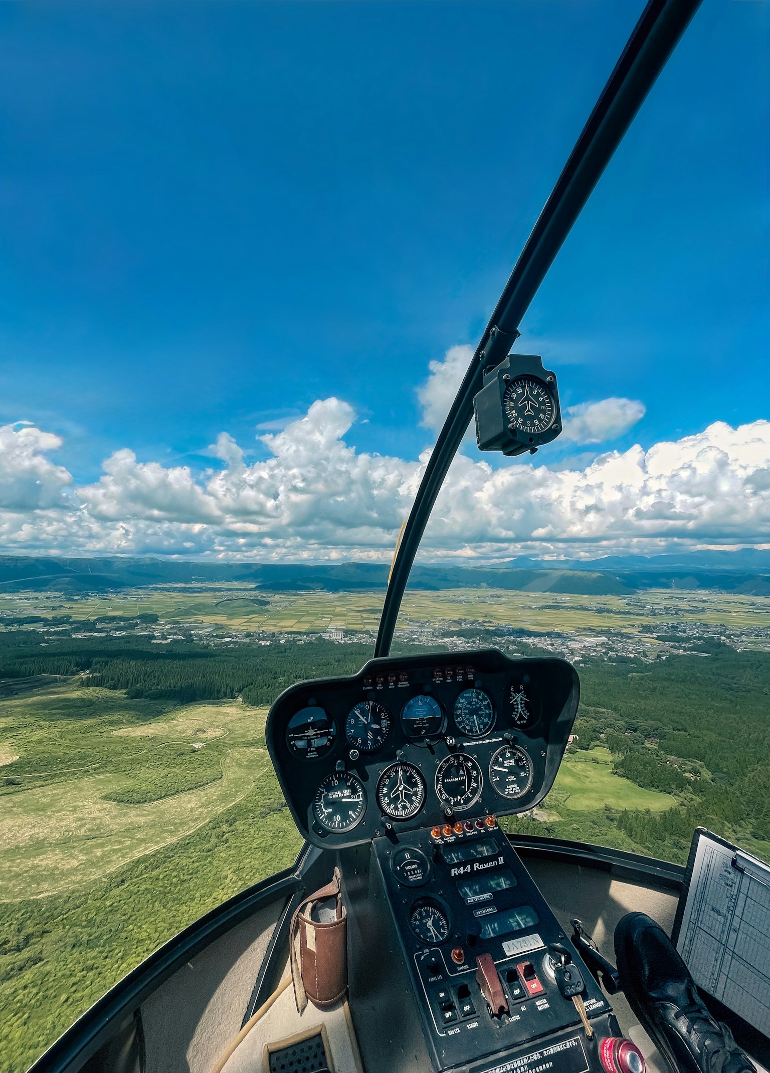 Vista desde la cabina de un helicóptero mostrando cielo azul y nubes sobre paisajes verdes