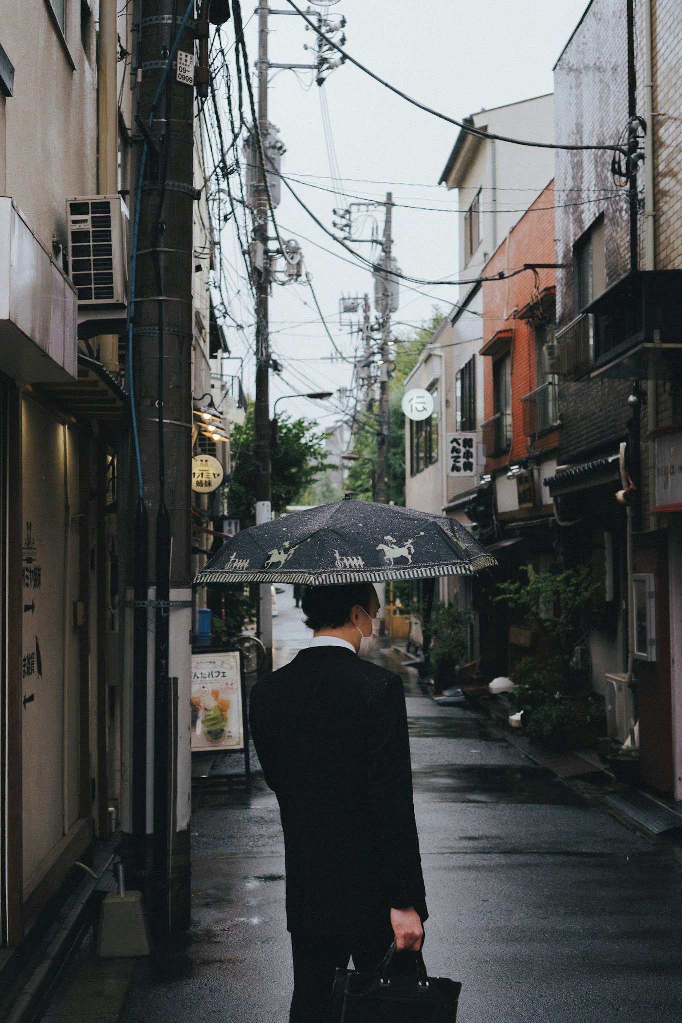 vista da dietro di una persona in abito che cammina in un vicolo di Tokyo