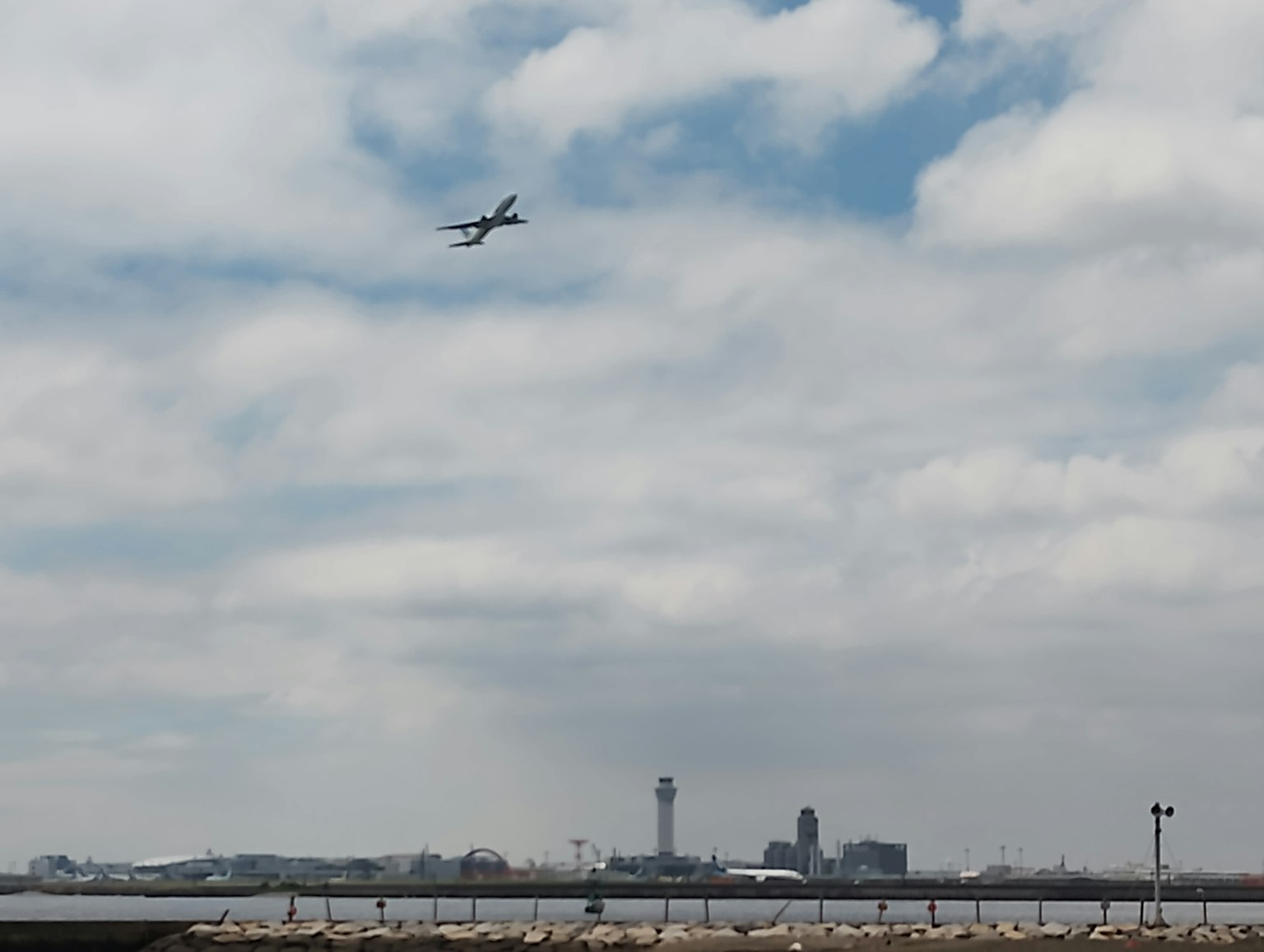 一架飛機在空中飛翔，背景是城市天際線和雲朵