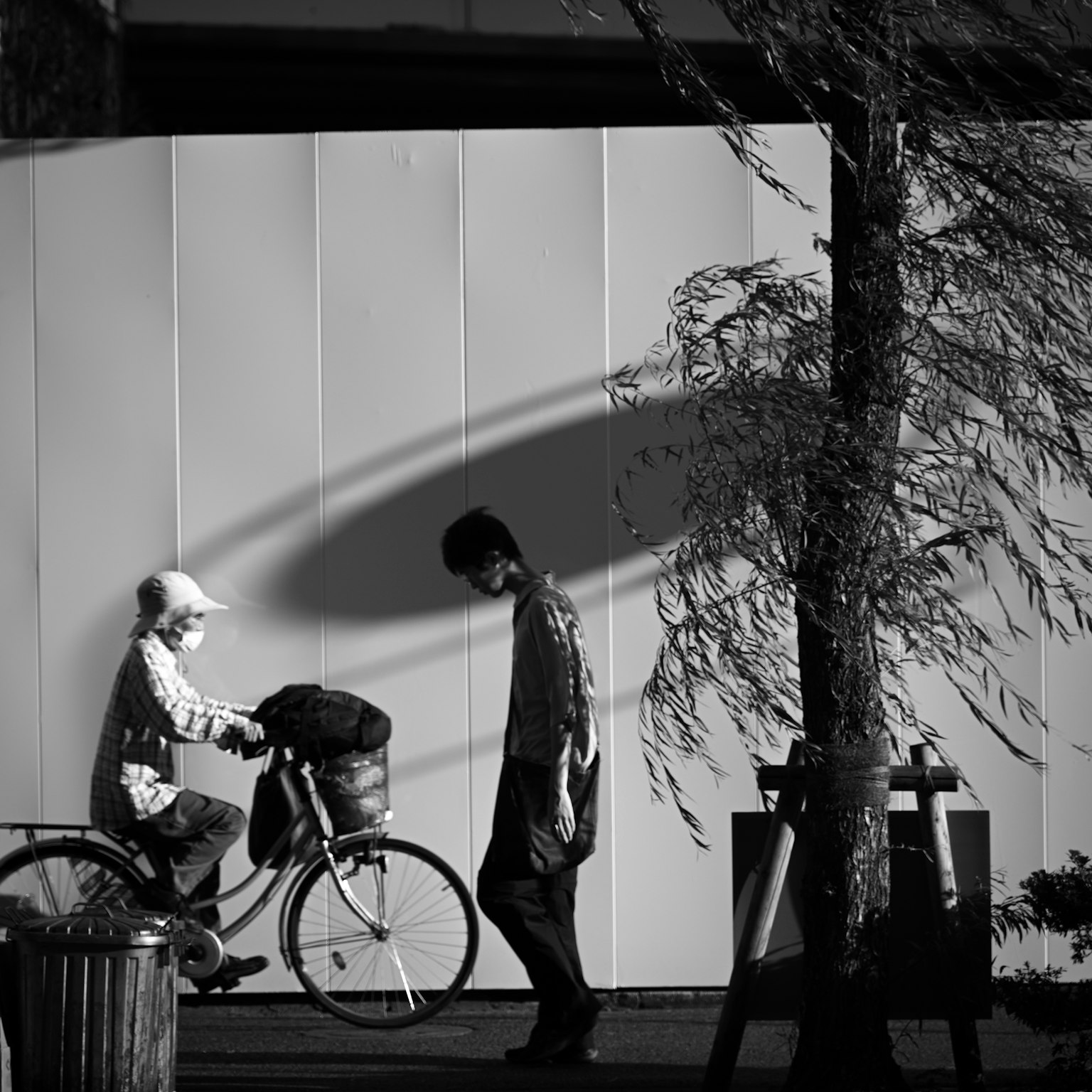 Silhouette d'un enfant à vélo et d'un homme marchant dans un coin de rue monochrome