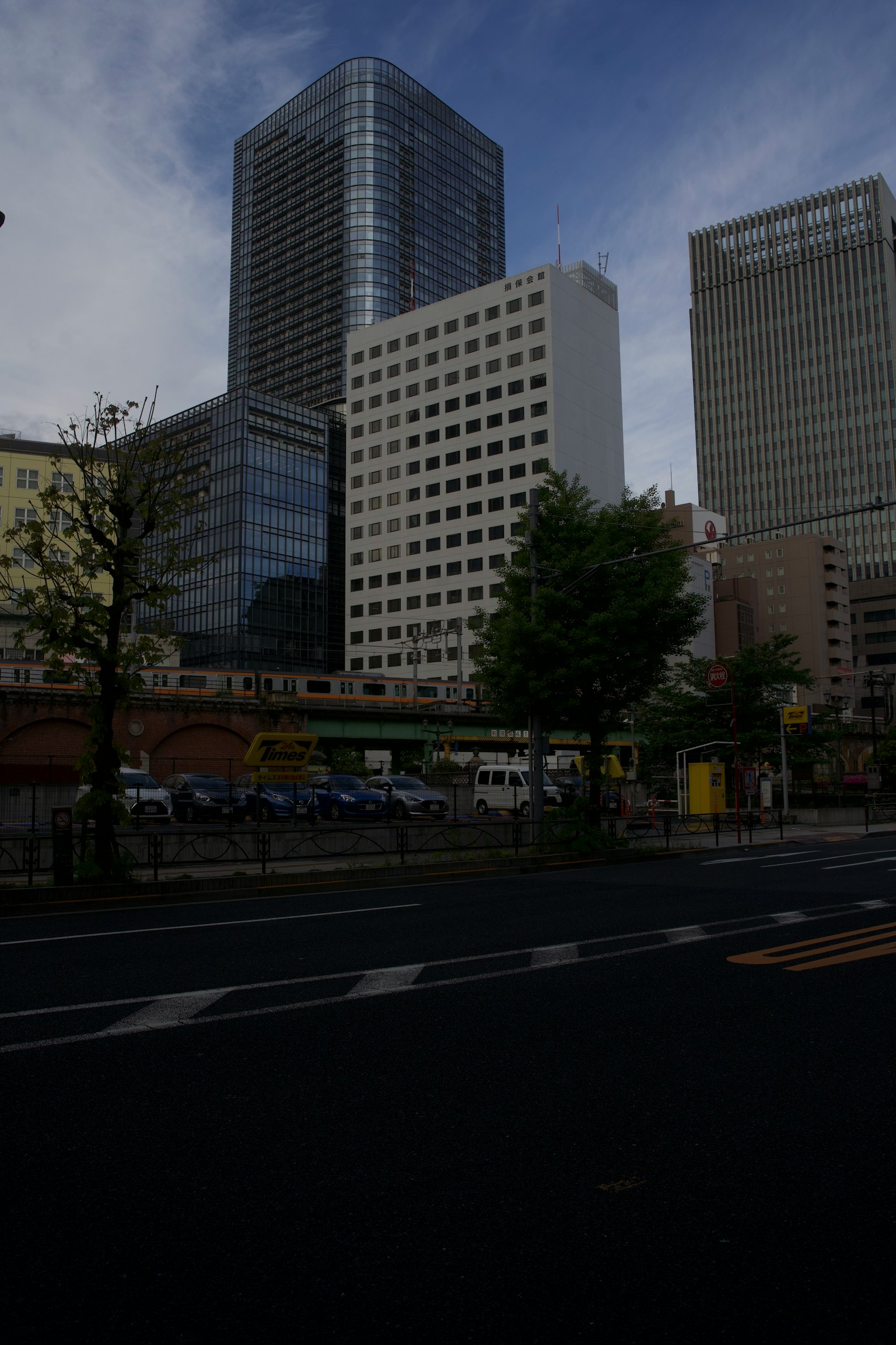 Urban skyline featuring tall buildings and a green tree under a cloudy sky