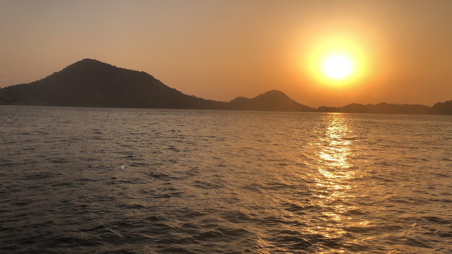 Atardecer sobre el océano con montañas al fondo reflejando la luz