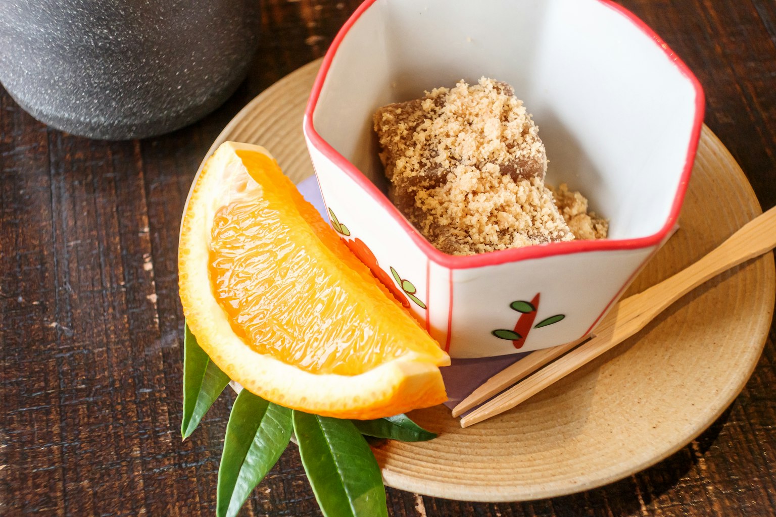 Japanese-style dish with a bowl containing a food item next to a slice of orange and leaves