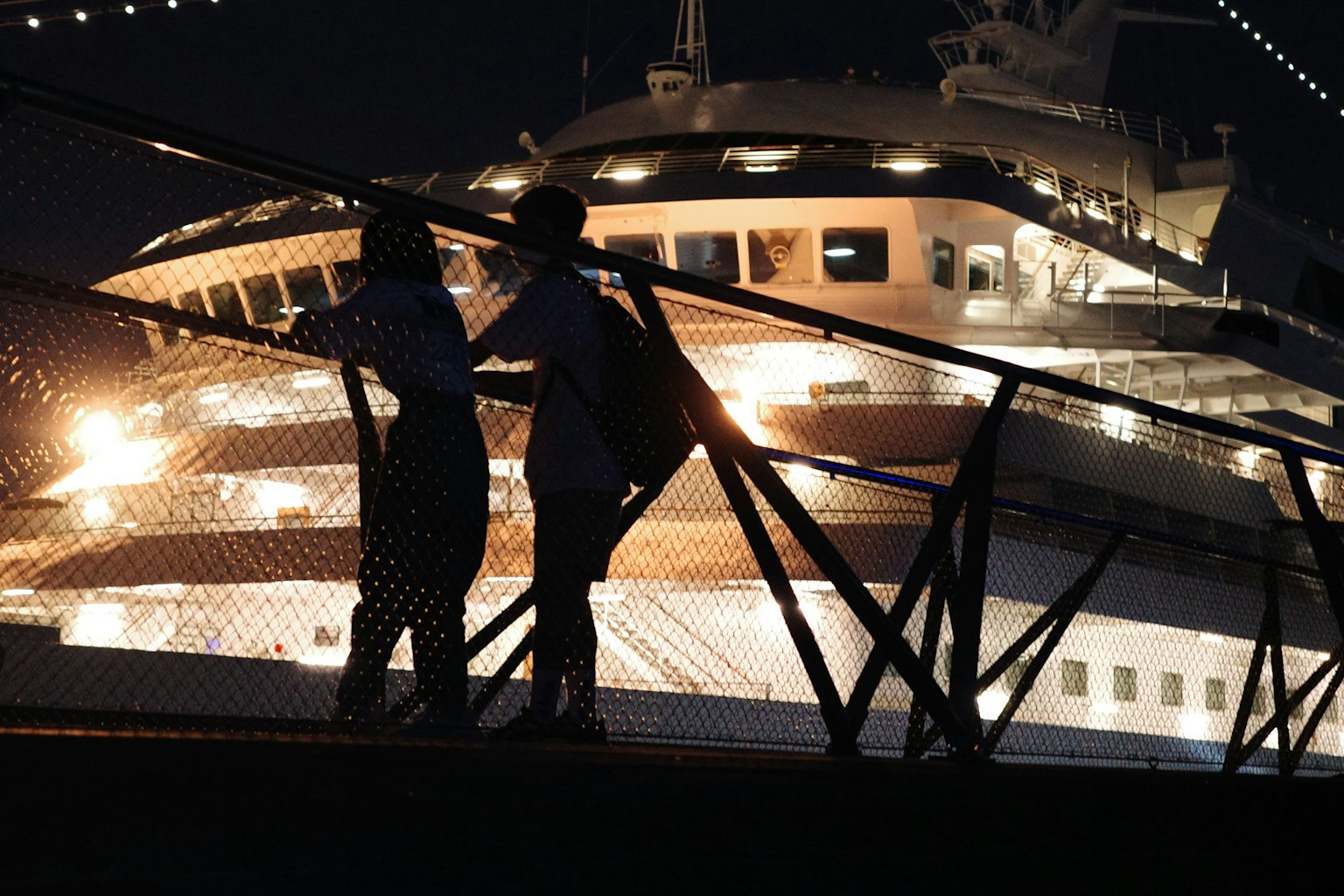 คู่รักที่มองเรือสำราญหรูในเวลากลางคืนพร้อมแสงไฟเมือง
