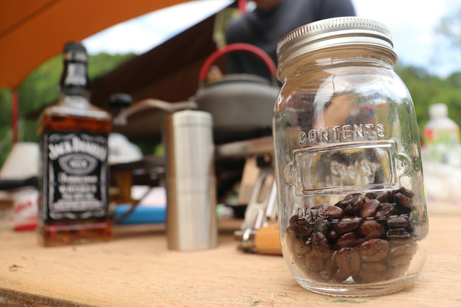 A glass jar filled with coffee beans and a bottle of Jack Daniel's on a camping table