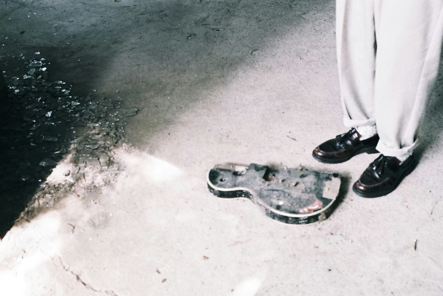 A broken guitar lying on the ground near a person's feet