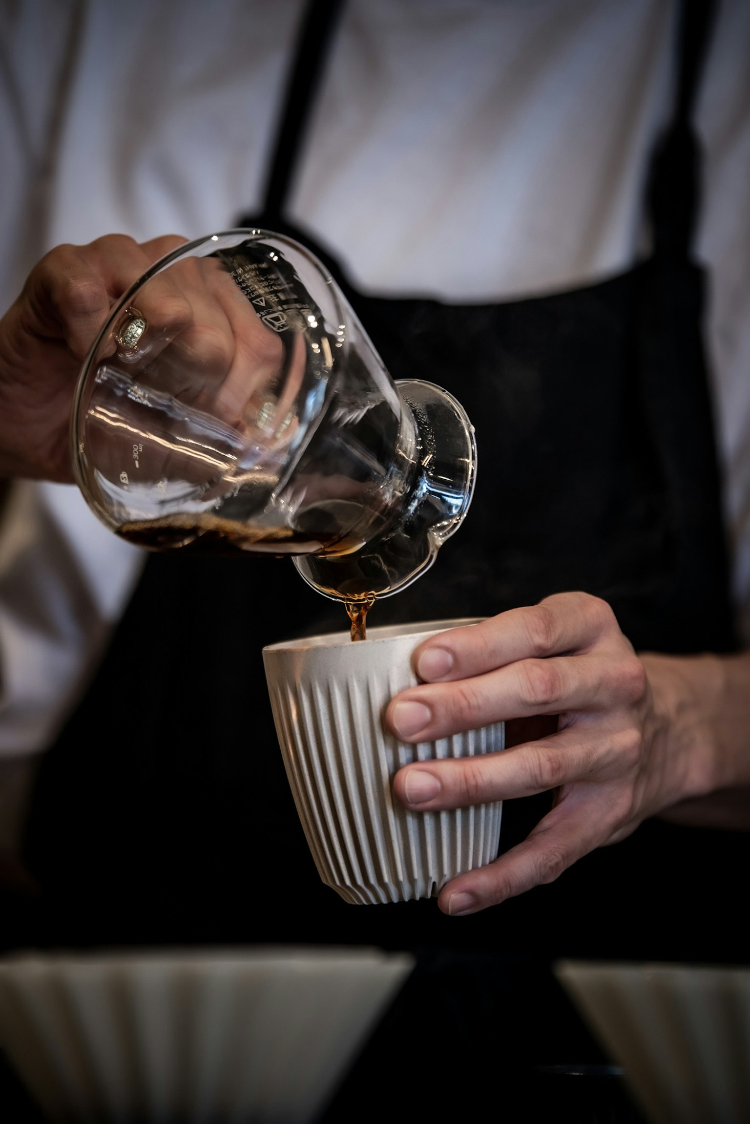 Barista versant du café dans une tasse artisanale avec une carafe en verre
