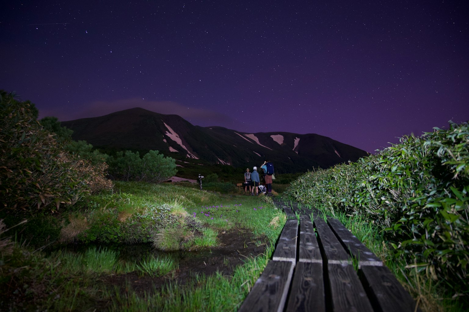 Pasarela de madera bajo un cielo estrellado con montañas al fondo