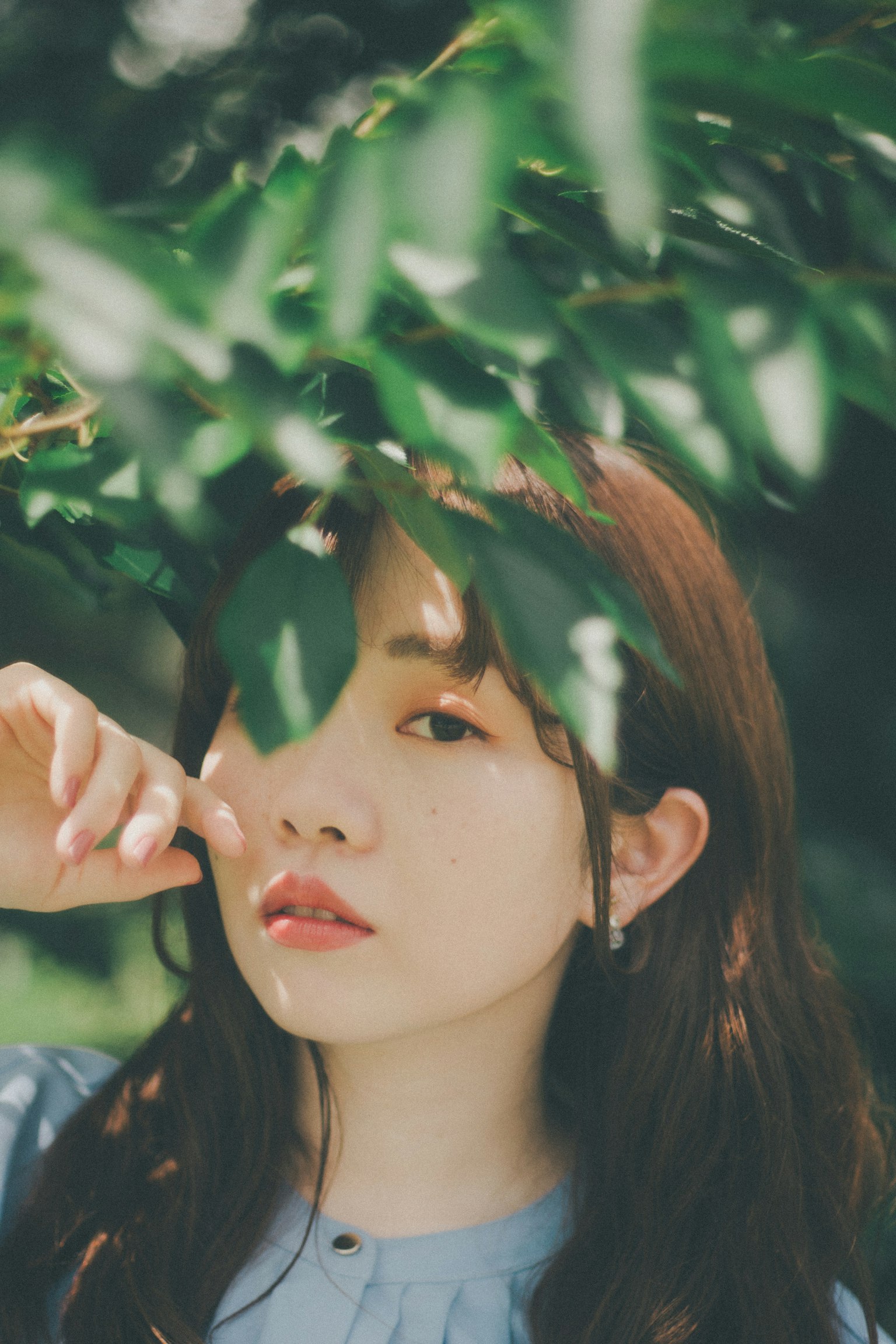 Khuôn mặt của người phụ nữ bị che khuất bởi lá xanh Biểu cảm nhẹ nhàng trong ánh sáng tự nhiên