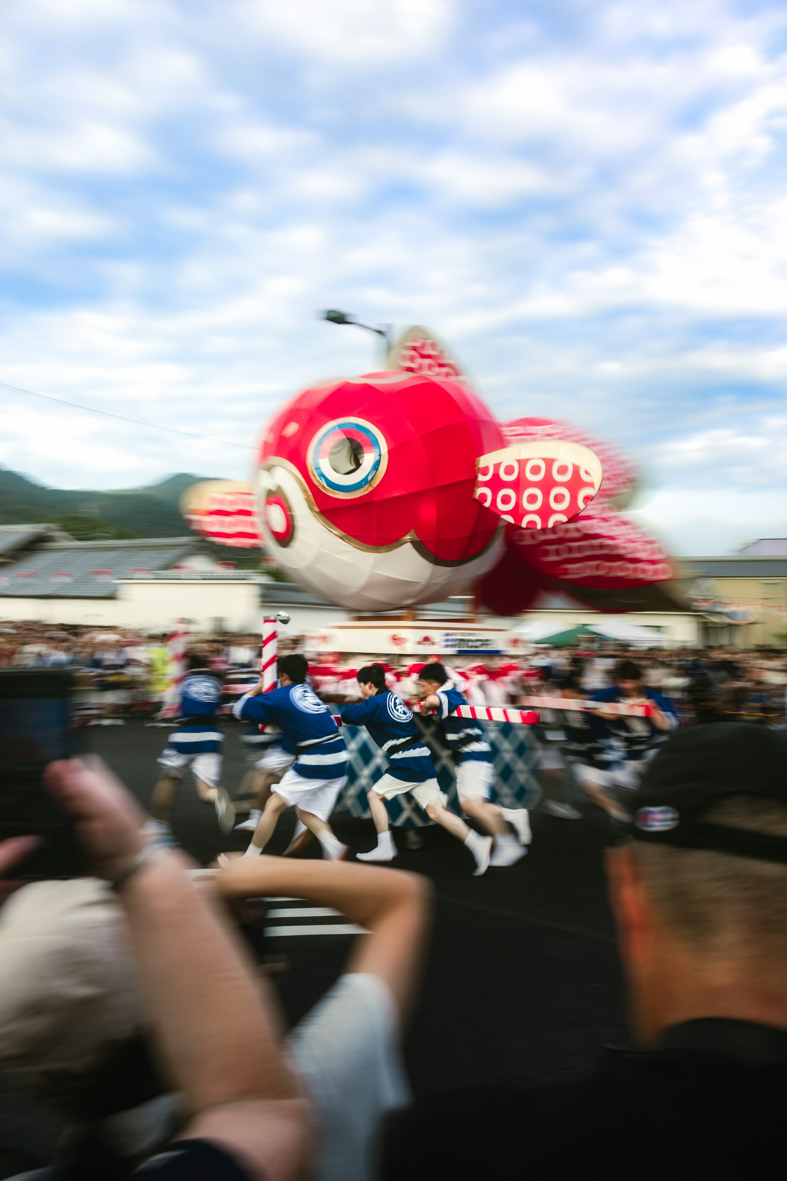 Red fish balloon floating at a festival with people dancing around