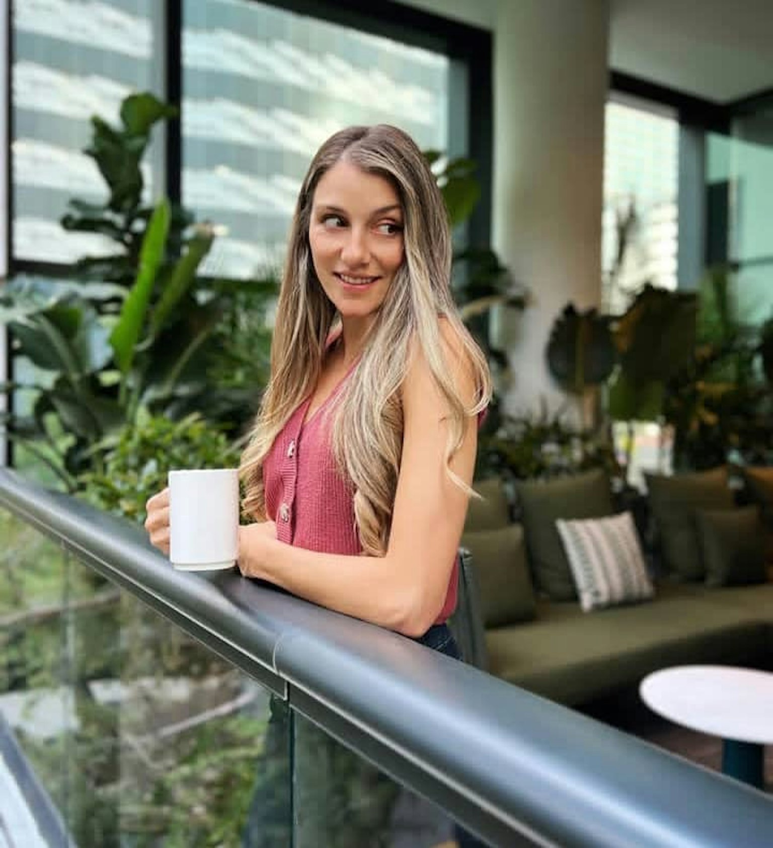 女性が植物に囲まれたカフェでコーヒーを持って微笑んでいる
