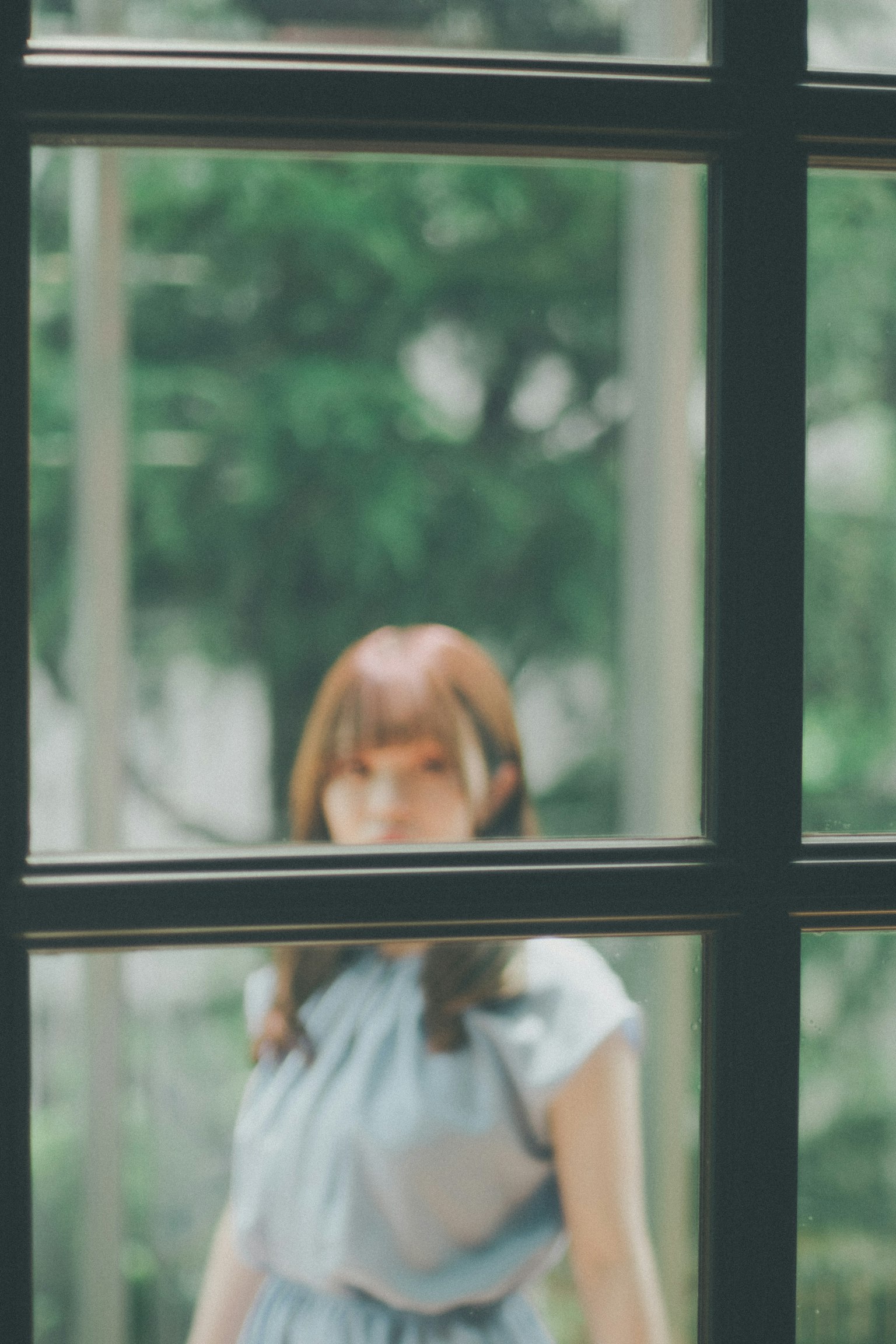 Vista sfocata di una donna attraverso una finestra con vegetazione sullo sfondo