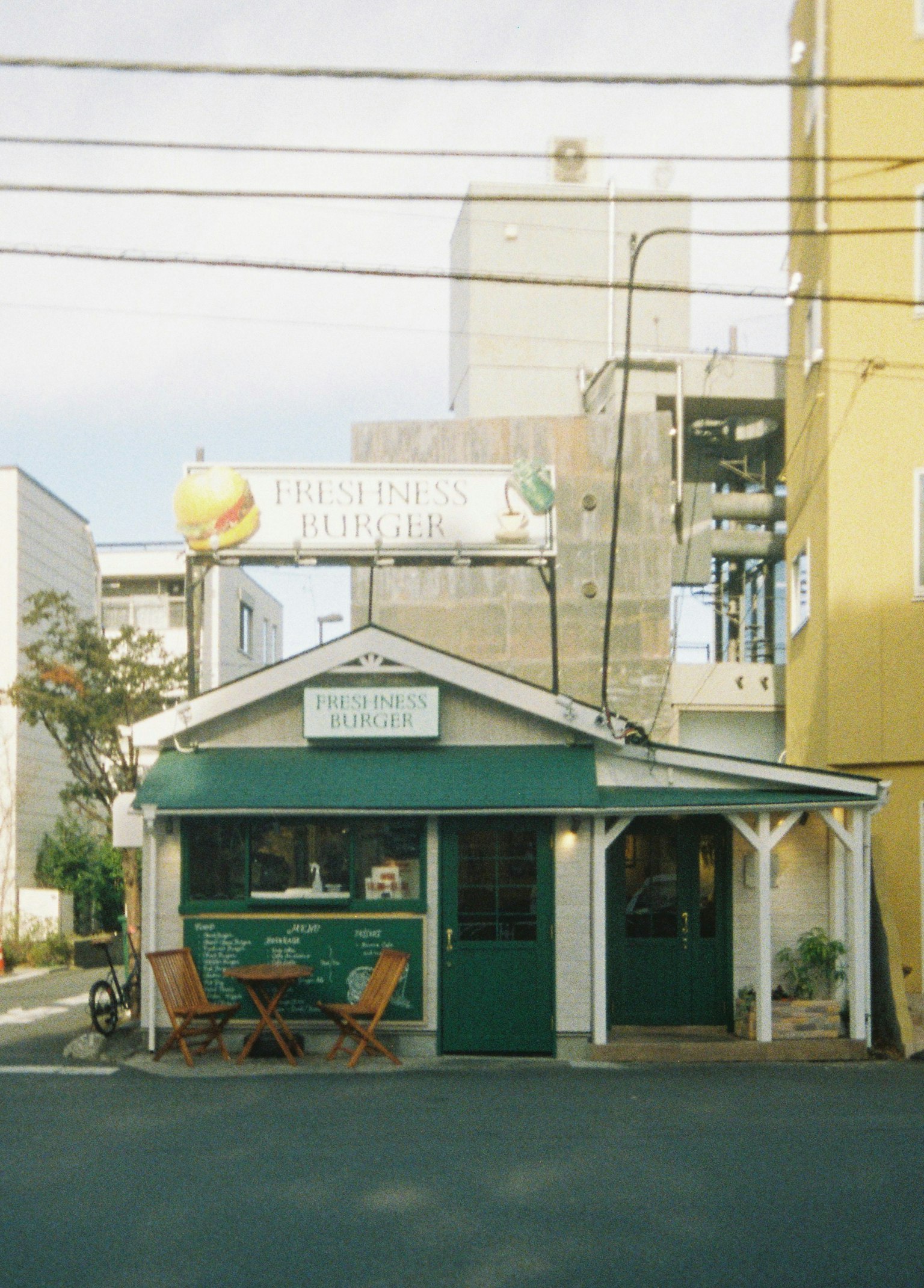 Charmantes grünes Café mit Außensitzplätzen und urbanem Hintergrund