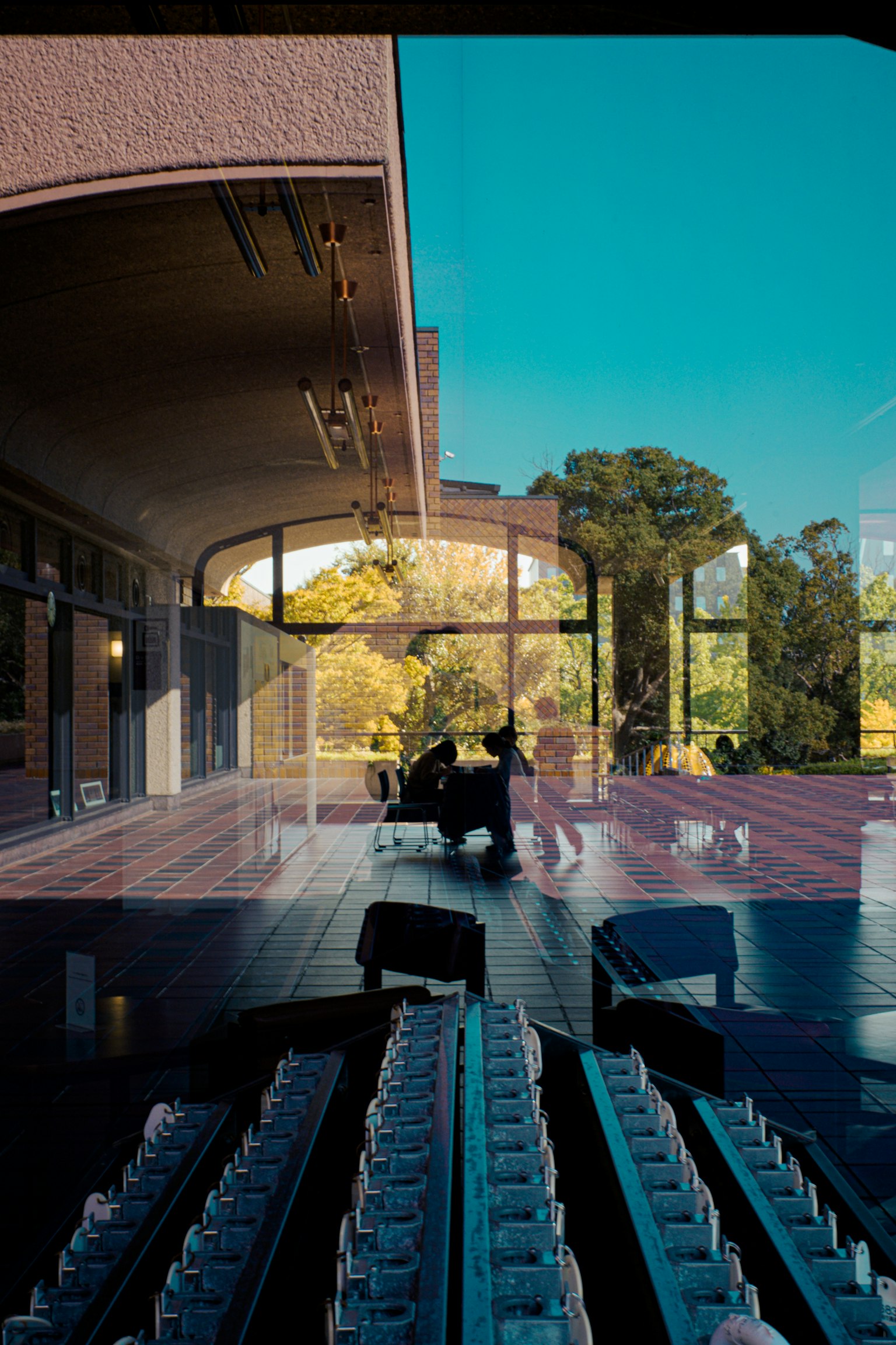 現代的な建物の内部と外部の景色が映る窓の前に座る人々