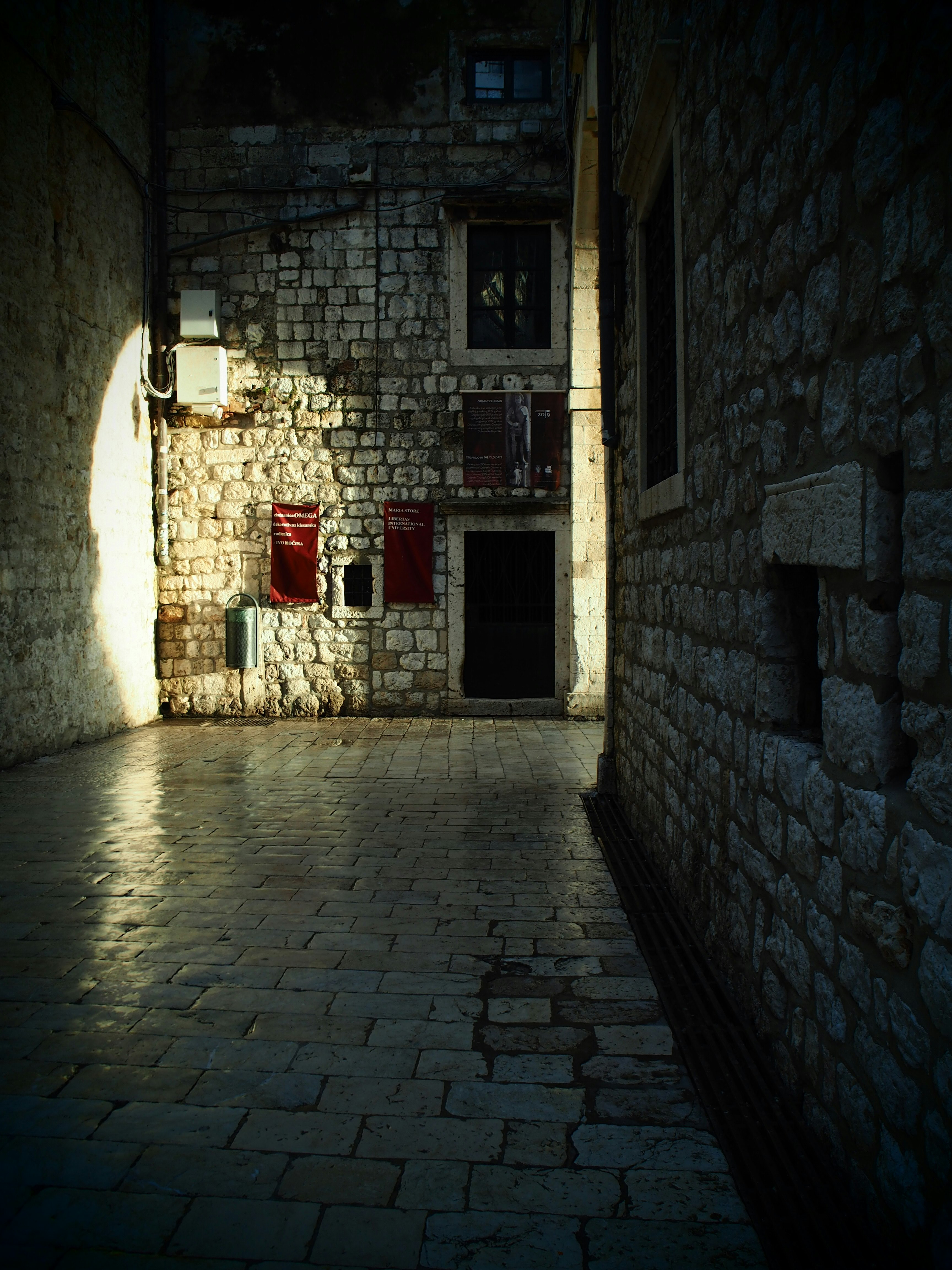 stone alleyway with light spilling onto cobblestones and old stone walls