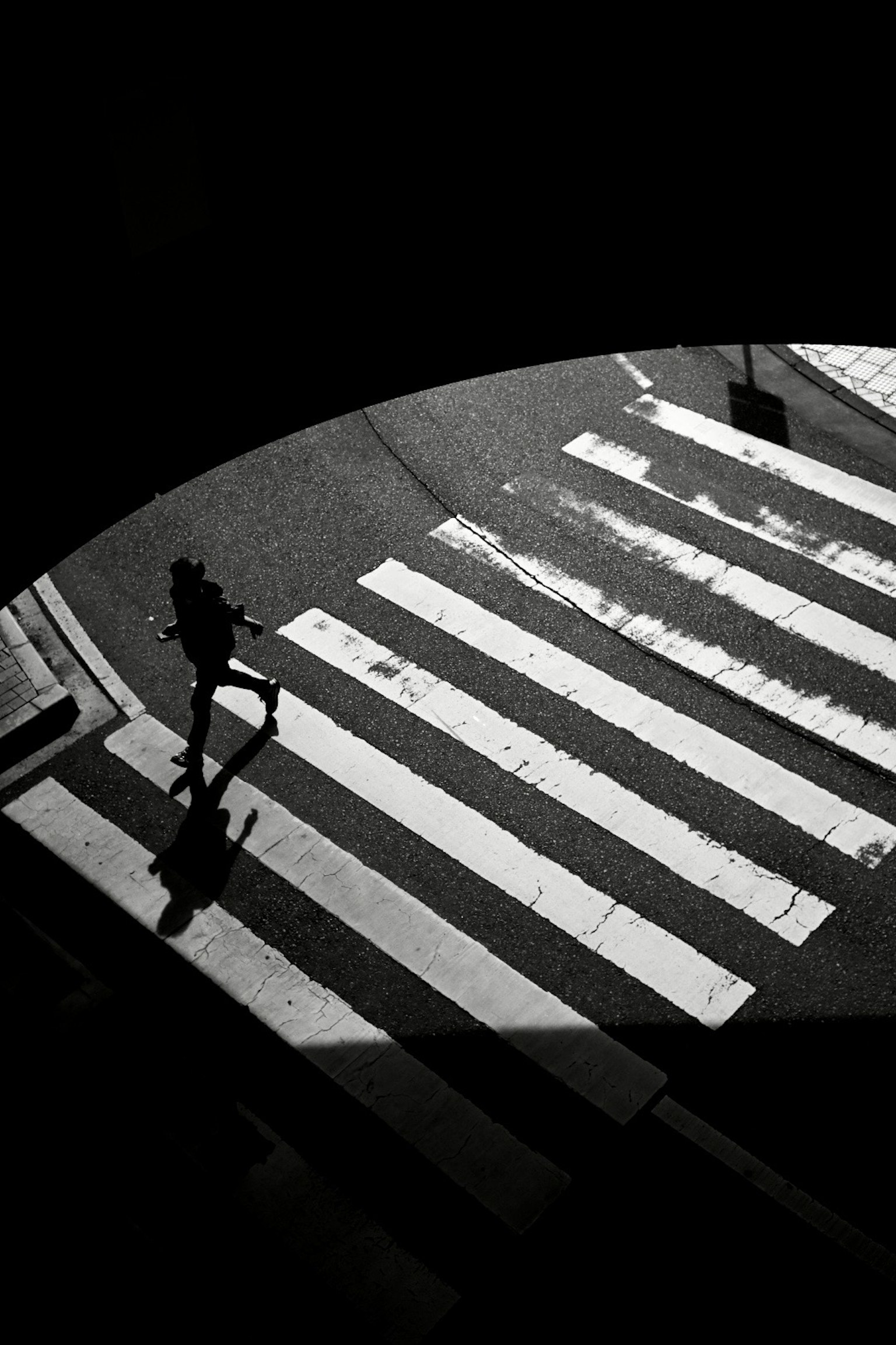 Silhouette di una persona che attraversa un attraversamento pedonale striato in bianco e nero