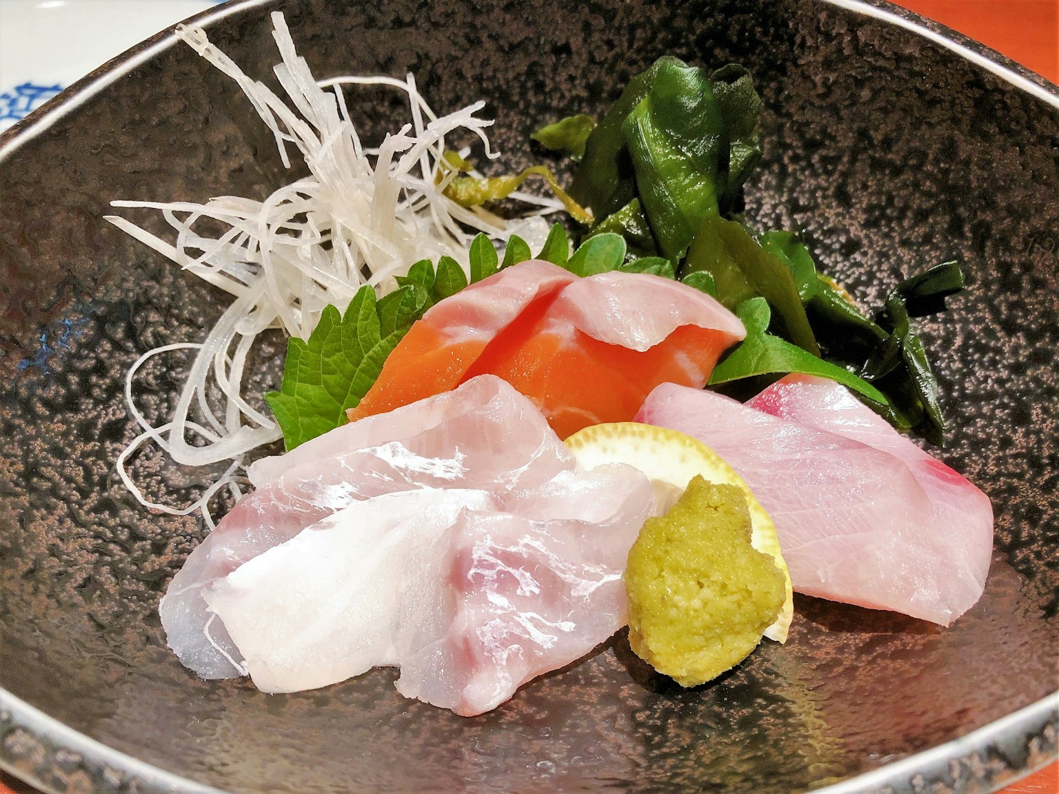 Fresh sashimi platter with sliced fish, garnished with shredded daikon and greens, served with wasabi and lemon