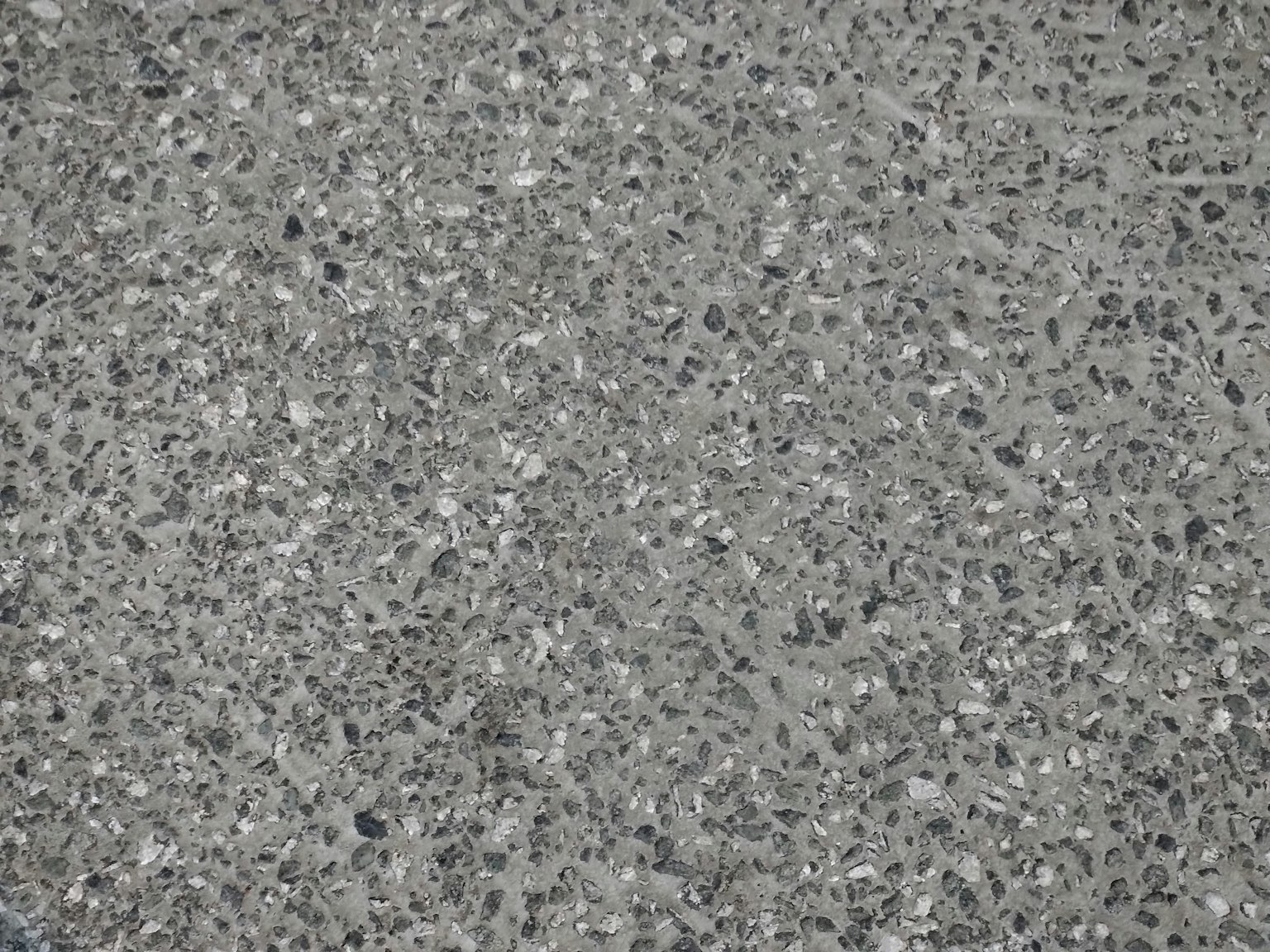 Gray concrete surface with small stones and particles visible
