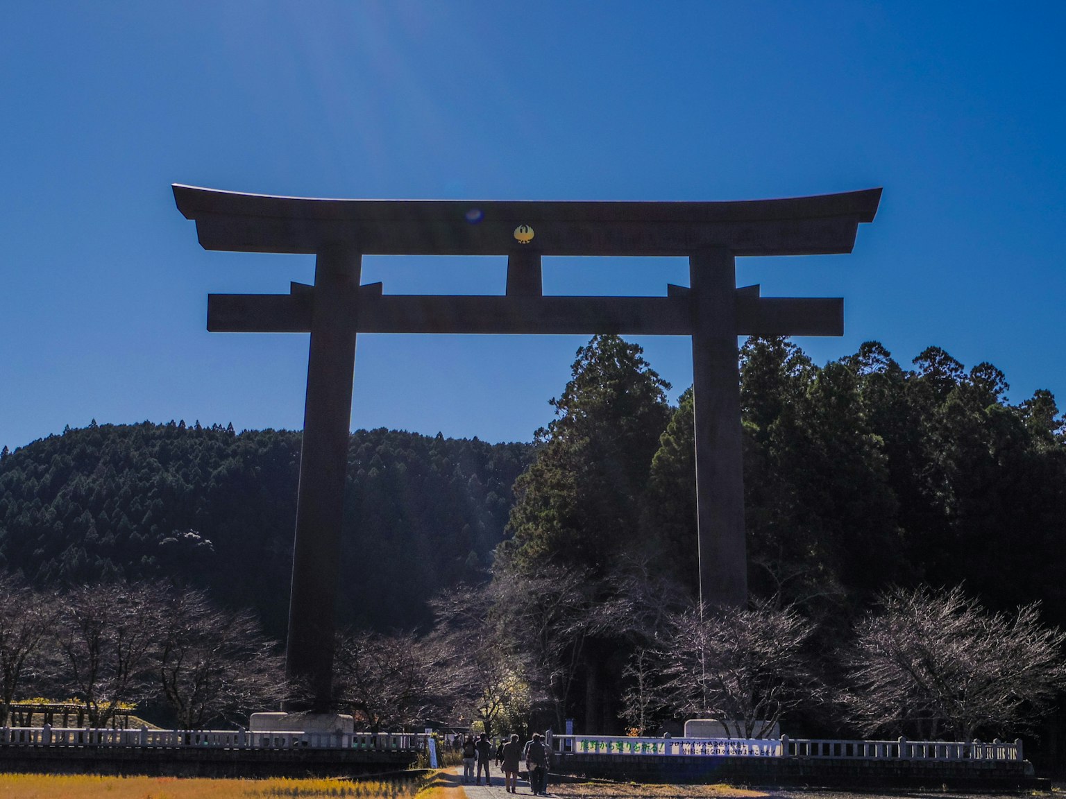Cổng torii lớn dưới bầu trời xanh trong vây quanh bởi cây cối và núi non