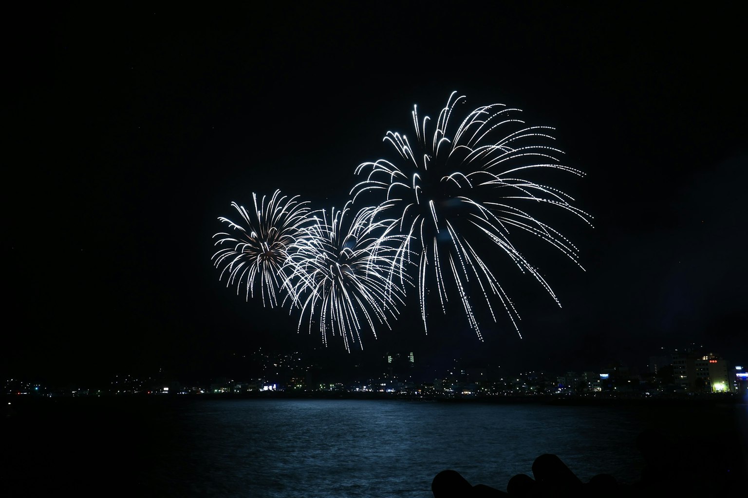 Bellissimo spettacolo di fuochi d'artificio bianchi che scintillano nel cielo notturno riflessi nell'acqua