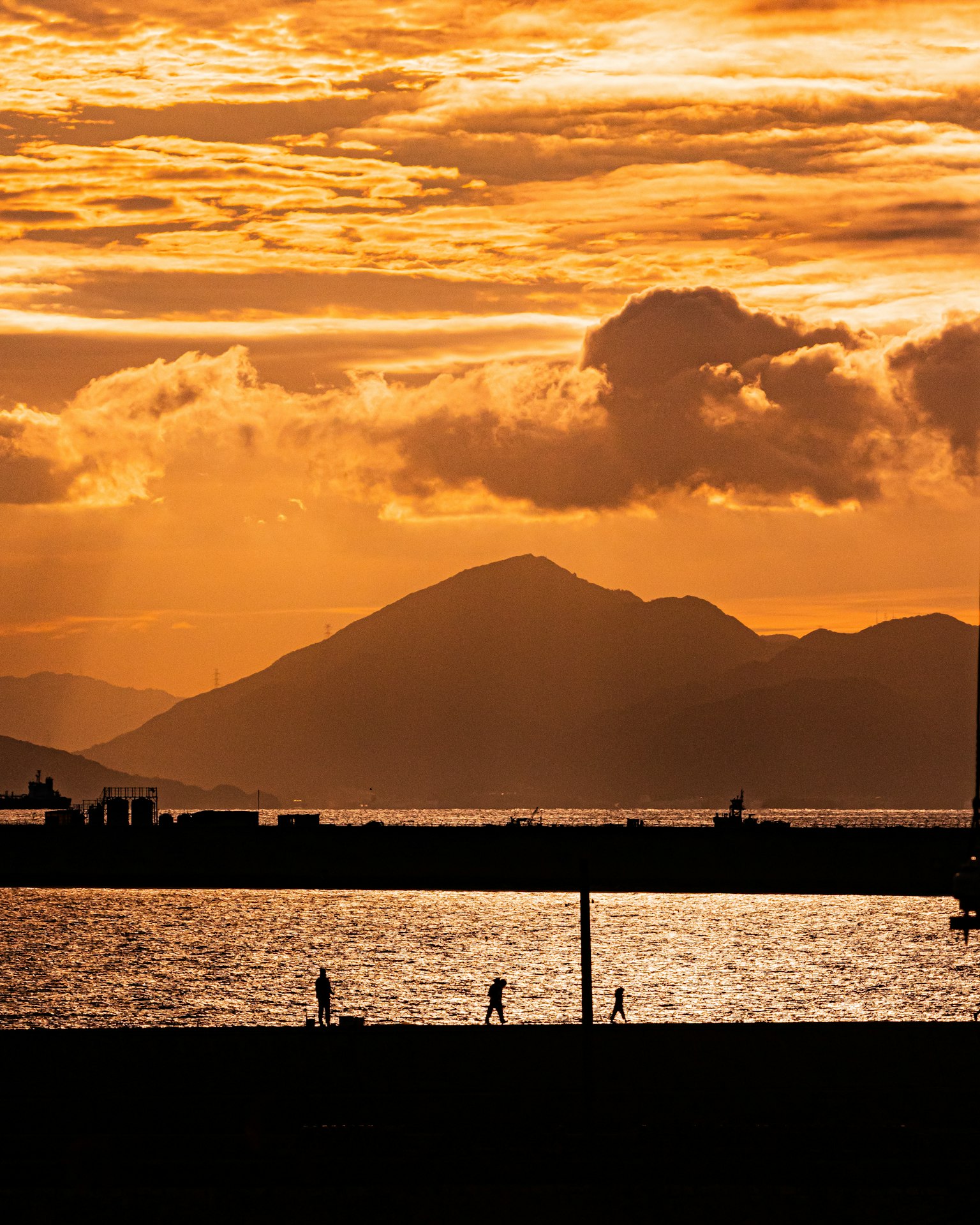 Silueta de personas caminando junto al mar con montañas y atardecer