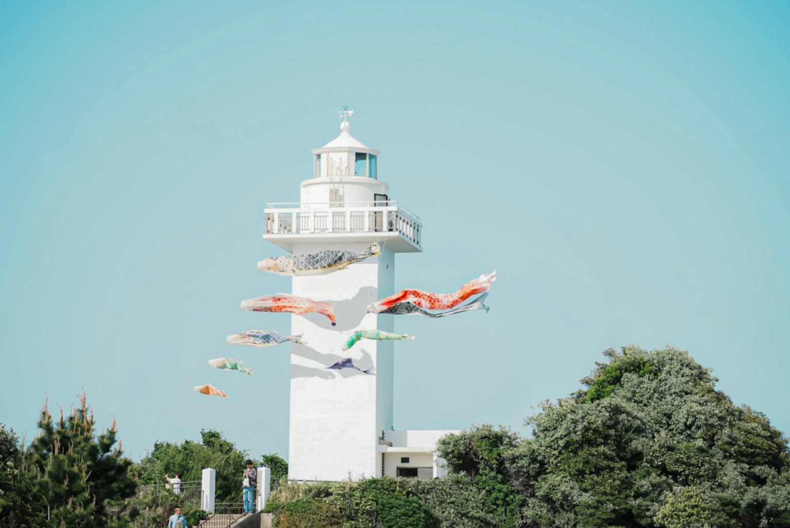 A white lighthouse with divers leaping off into the air against a clear blue sky