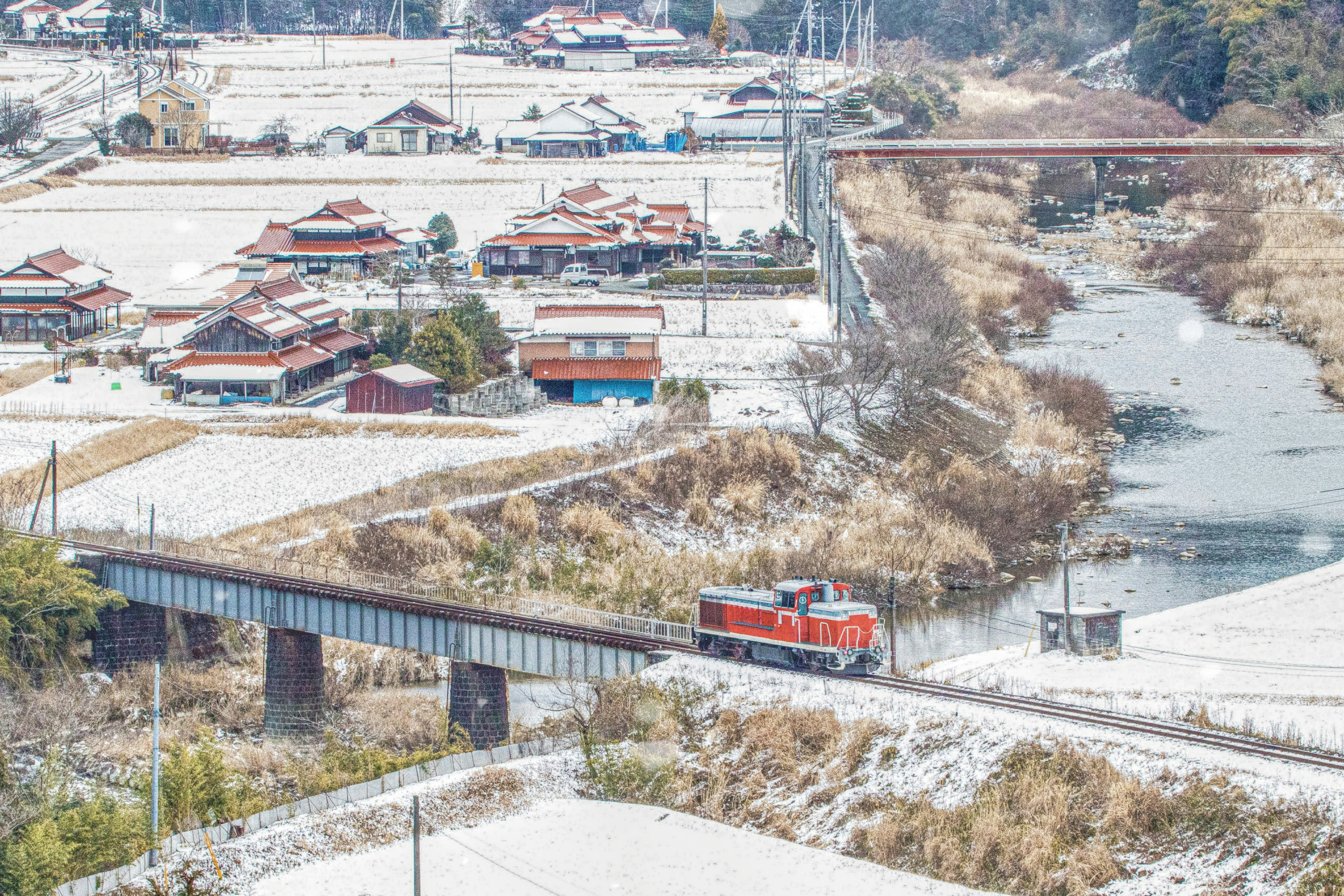 雪の線路沿いに広がる川と集落の風景