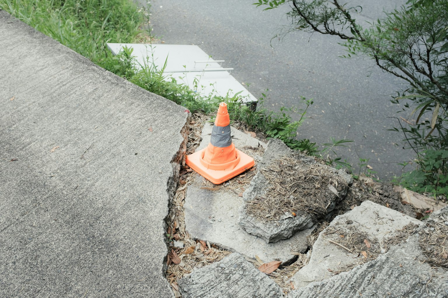 Cono stradale arancione posizionato su cemento crepato al bordo di una strada