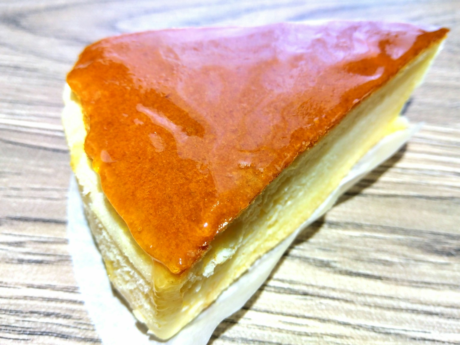 Ein Stück dreieckiger Kuchen mit glänzendem Karamellbelag cremiger Füllung auf einem Holztisch