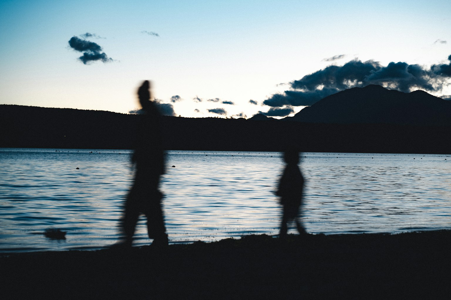 夕暮れ時の湖のほとりを歩く人々のシルエット