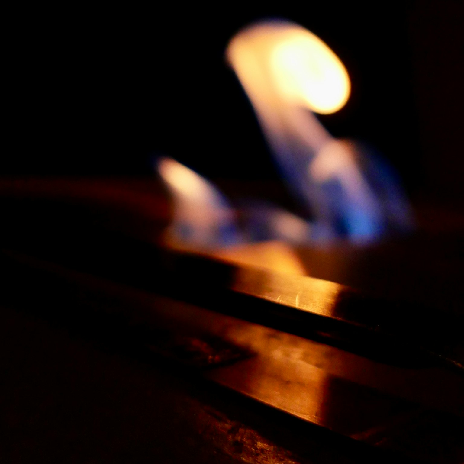 Flickering blue and orange flames against a dark background reflecting on a metallic surface